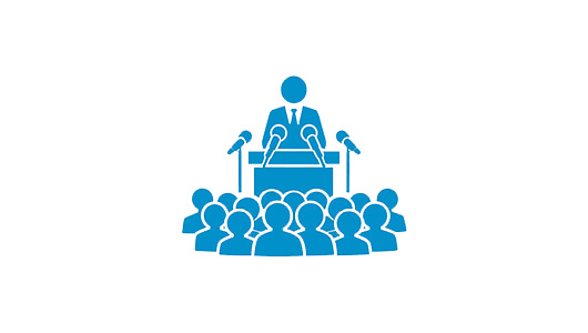 Ein Symbol einer Person die vor einem Rednerpult steht und in Mikrofone spricht. Davor steht eine Gruppe Menschen.